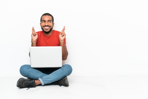 Jonge Ecuadoraanse man met een laptop zittend op de vloer geïsoleerd op een witte achtergrond met vingers over elkaar