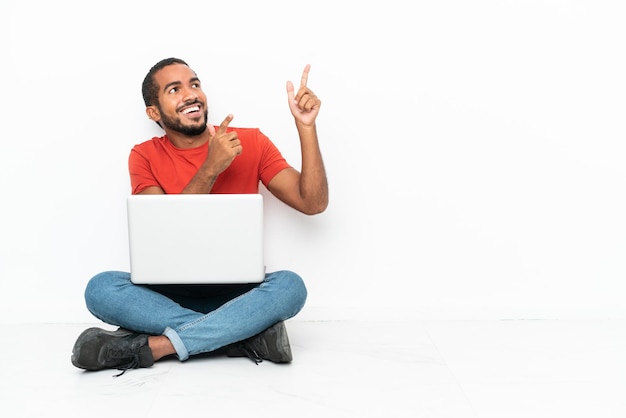 Jonge Ecuadoraanse man met een laptop zittend op de vloer geïsoleerd op een witte achtergrond wijzend met de wijsvinger een geweldig idee