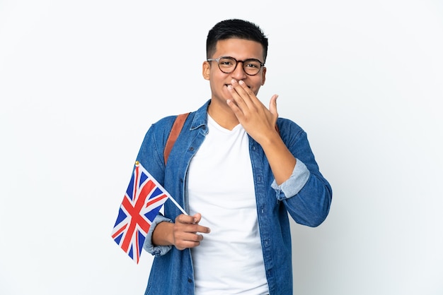 Jonge Ecuadoraanse vrouw die een vlag van het Verenigd Koninkrijk houdt die op witte achtergrond wordt geïsoleerd gelukkig en glimlachend die mond met hand behandelen