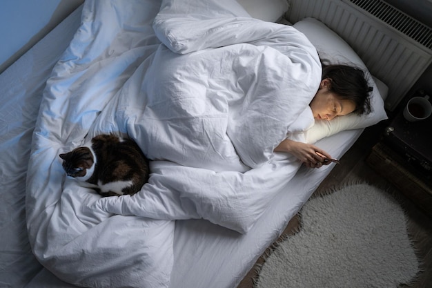 Jonge eenzame depressieve vrouw die smartphone gebruikt terwijl ze 's nachts alleen in bed ligt met een kat erin