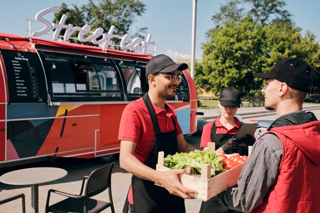 Jonge eigenaar van een straatvoedselwagen die een doos met verse groenten neemt