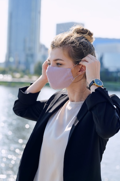 Jonge elegante blonde zakenvrouw in formalwear die een beschermend masker opzet voordat ze naar een ontmoeting met een collega of een afspraak met de klant gaat