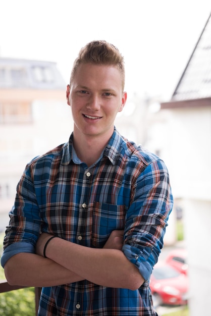 Foto jonge elegante mode man staande op balkon met gekruiste armen en glimlachend