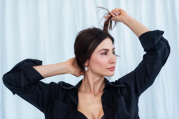 Jonge elegante vrouw houdt haar op een witte gordijnachtergrond