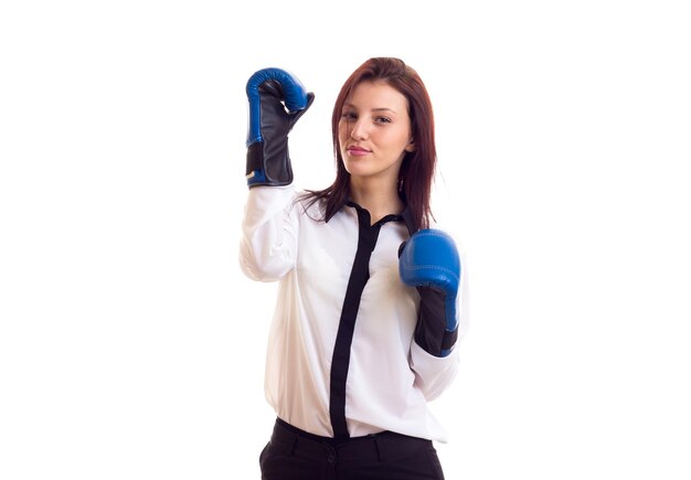 Jonge elegante vrouw in wit overhemd en zwarte broek met donker haar en blauwe bokshandschoenen op witte achtergrond in studio