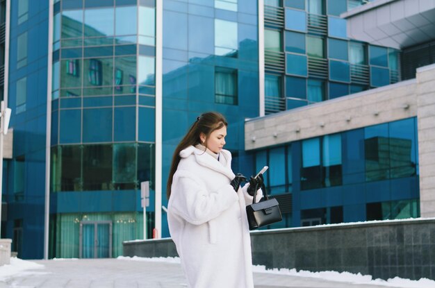 jonge elegante zakenvrouw in casual winterkleding, witte jas. Lopen. stadsstraat, praten