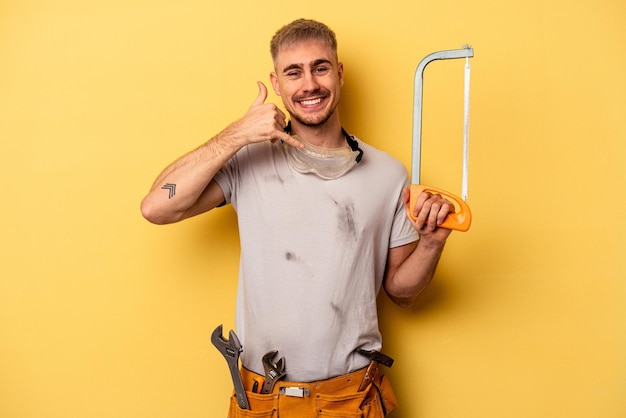 Jonge elektricien blanke man geïsoleerd op gele achtergrond met een mobiel telefoongesprek gebaar met vingers.