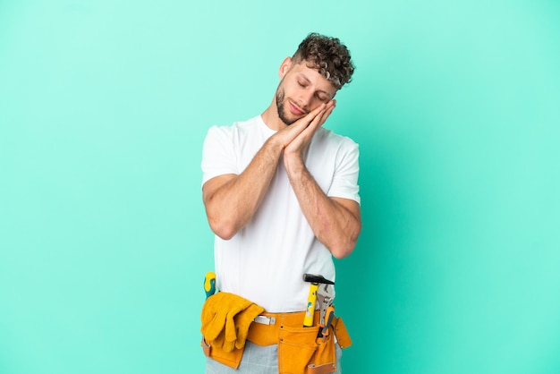 Jonge elektricien blonde man geïsoleerd op groene achtergrond slaap gebaar maken in dorable expression