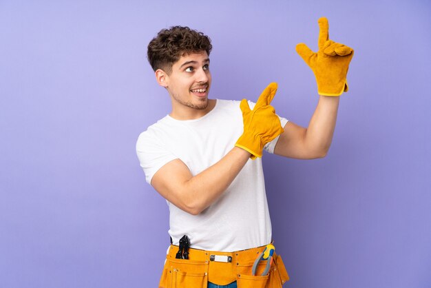 Jonge elektricien man meer dan geïsoleerd op paars wijzend met de wijsvinger een geweldig idee