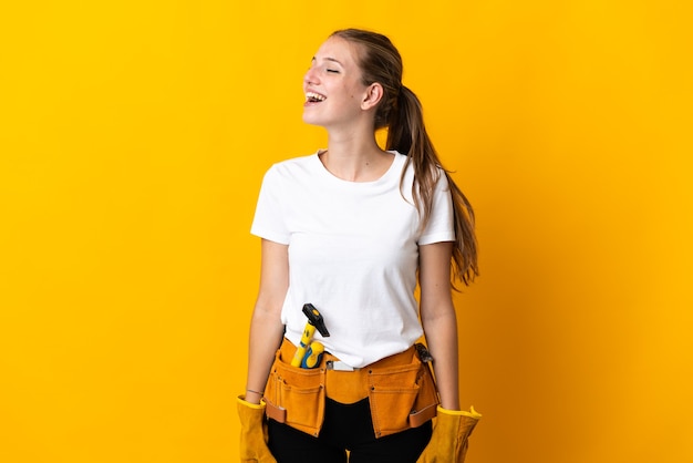 Jonge elektricienvrouw die op geel wordt geïsoleerd dat in zijpositie lacht
