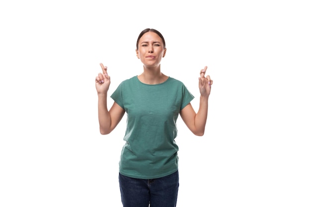 Jonge emotionele brunette vrouw in t-shirt en jeans kruiste haar vingers