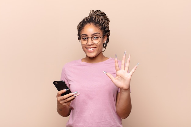 Jonge en afrovrouw die vriendelijk glimlacht kijkt, nummer vijf of vijfde met vooruit hand toont, aftellend. slimme telefoon concept