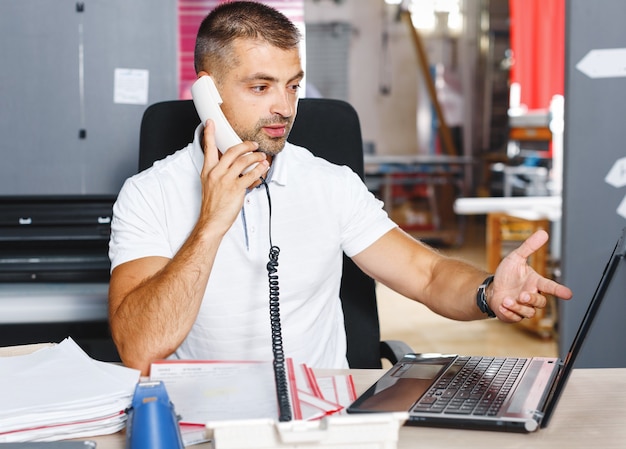 Jonge en ambitieuze beurshandelaar doet een deal via de telefoon in een druk kantoor vol computers.