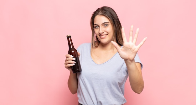 Jonge en blonde vrouw die vriendelijk glimlacht kijkt, nummer vijf of vijfde met vooruit hand toont, aftellend