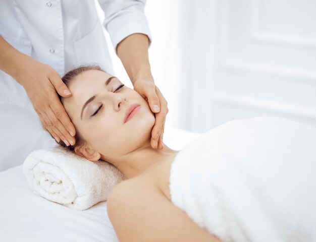 Jonge en blonde vrouw genieten van gezichtsmassage in spa salon Beauty concept