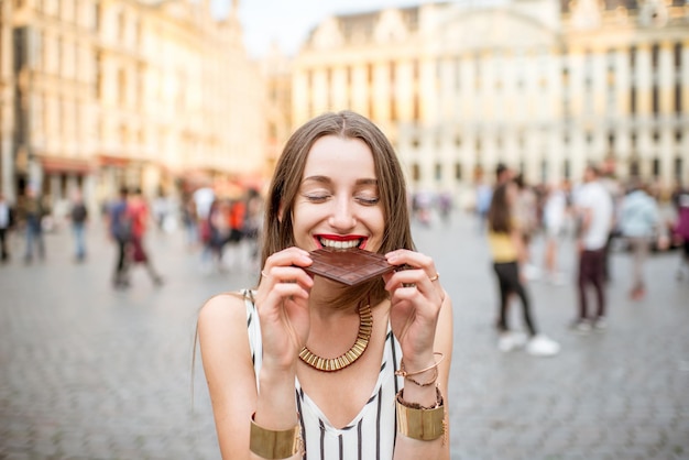 Jonge en gelukkige vrouw met donkere chocoladereep die buiten staat op de Grote Markt in Brussel in België. België staat bekend om zijn chocolade