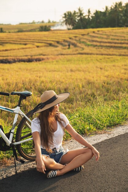 Jonge en gelukkige vrouw met een fiets aan kant van de weg