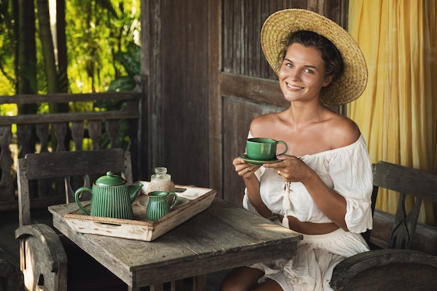 Jonge en gelukkige vrouw zittend op het zomerterras en koffie drinken