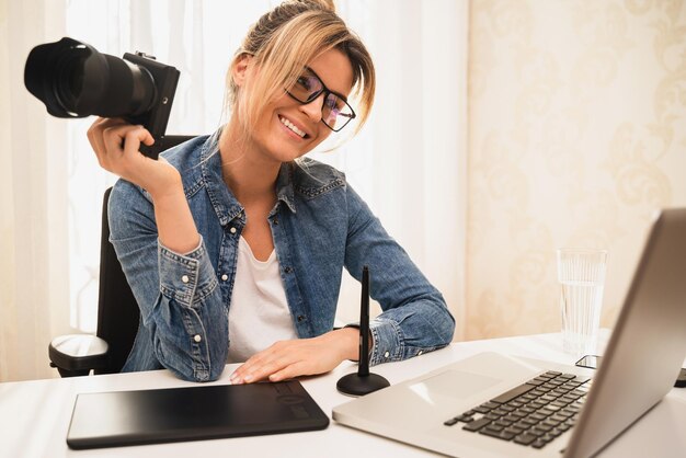 Jonge en gelukkige vrouwenfotograaf met een spiegelloze camera op de werkplek