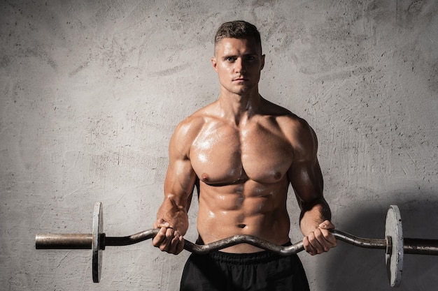 Jonge en gespierde bodybuilder trainen met een barbell tegen betonnen muur