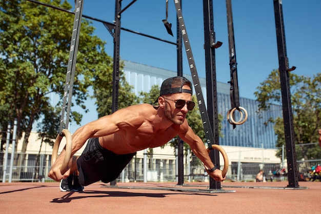 Jonge en knappe man doet wat push-ups. Hij gebruikt daarvoor loops