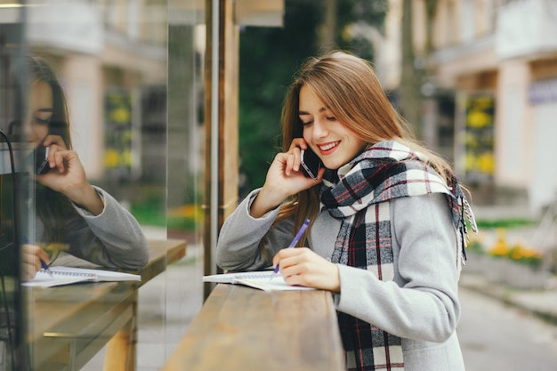 Jonge en mooie gilr staat in de buurt van het bouwen in een stad en gebruik de telefoon