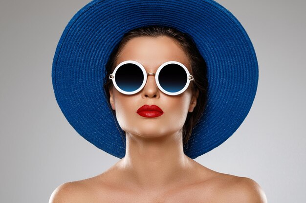 Jonge en mooie vrouw met blauwe hoed en zonnebril is klaar voor vakantie