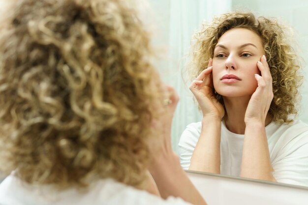 Jonge en mooie vrouw met krullend haar die in de spiegel in een badkamer kijkt