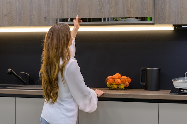 Jonge en mooie vrouw opent meubeldeur in moderne grijze keuken