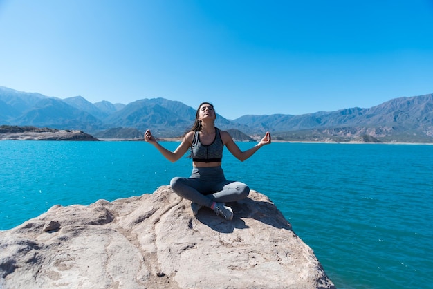 Jonge en mooie vrouw zitten mediteren op een meer tussen de bergen yoga