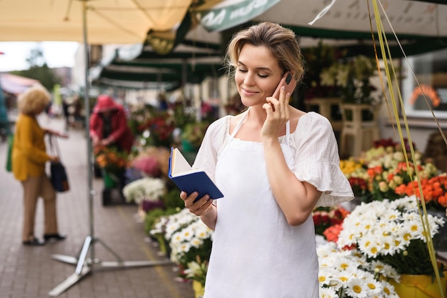 Jonge en mooie vrouwelijke bloemist die telefonisch de bestelling opneemt in haar kleine bloemenwinkel