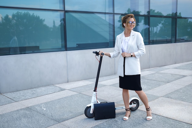 Jonge en mooie zakenvrouw rijdt elektrische scooter in de stad