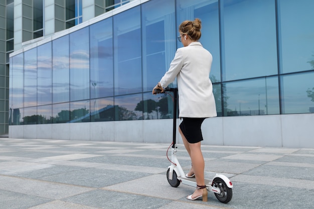 Jonge en mooie zakenvrouw rijdt elektrische scooter in de stad