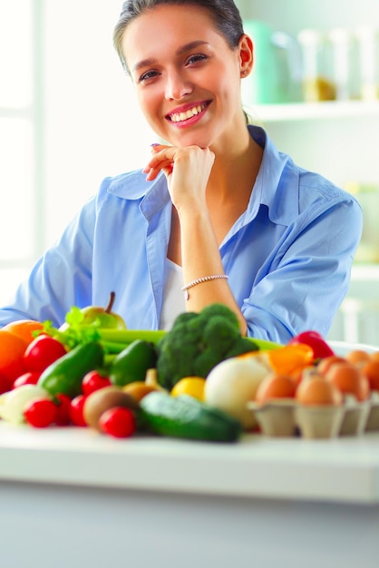 Jonge en schattige vrouw zittend aan de tafel vol groenten en fruit in het houten interieur