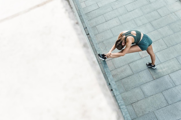 Jonge en sportieve vrouw rekt zich uit tijdens fitnesstraining buitenshuis