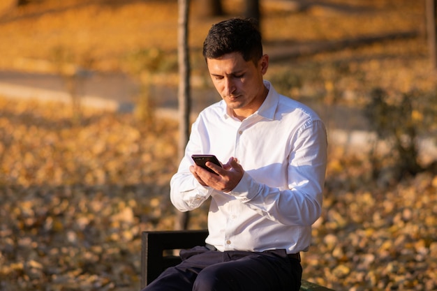 Jonge en succesvolle zakenman die in het park staat en een bericht leest op zijn smartphone. Zakelijk portret.