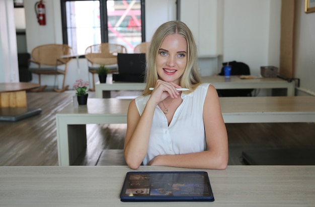 Jonge en vrolijke vrouw die op digitale tablet werkt met draadloos internet terwijl ze ontspannen zit in café. Concept van vrije tijd, freelance en mobiel werk