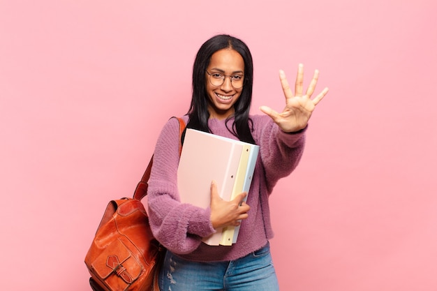 Jonge en zwarte vrouw die vriendelijk glimlacht kijkt, nummer vijf of vijfde met vooruit hand toont, aftellend. student concept