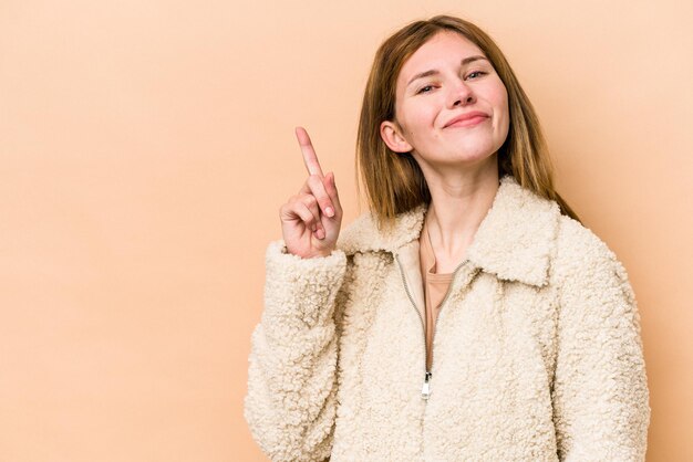 Jonge Engelse die vrouw op beige achtergrond wordt geïsoleerd die nummer één met vinger toont.