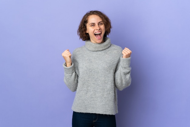 Jonge Engelse die vrouw op purpere achtergrond wordt geïsoleerd die een overwinning in winnaarpositie viert