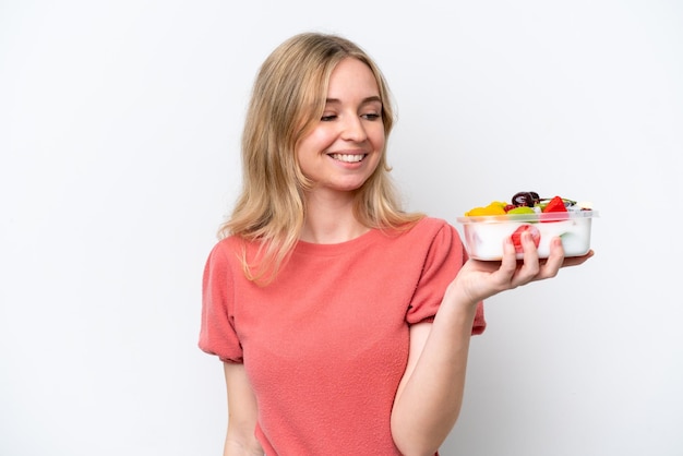 Jonge Engelse vrouw die een kom fruit over een geïsoleerde witte achtergrond houdt met een gelukkige uitdrukking