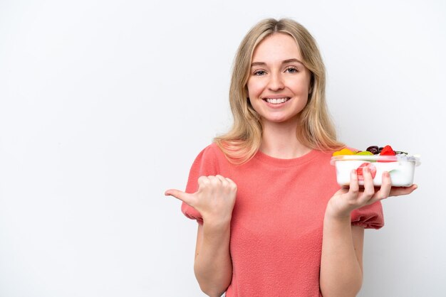 Jonge Engelse vrouw die een schaal met fruit vasthoudt over een geïsoleerde witte achtergrond die naar de zijkant wijst om een product te presenteren