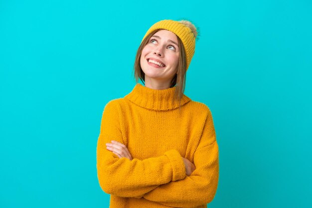 Jonge Engelse vrouw die een winterjas draagt die op een blauwe achtergrond wordt geïsoleerd terwijl ze glimlacht