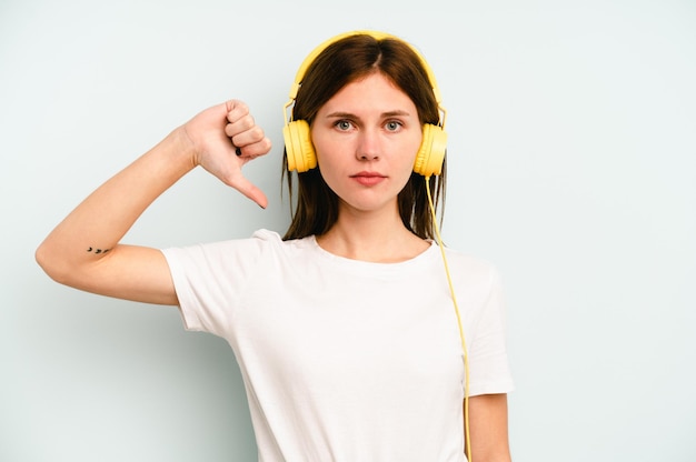 Jonge Engelse vrouw die naar muziek luistert geïsoleerd op een blauwe achtergrond met een afkeergebaar, duim omlaag. Onenigheid begrip.