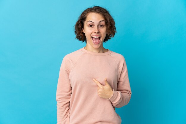 Jonge Engelse vrouw die op blauwe achtergrond met verrassingsgelaatsuitdrukking wordt geïsoleerd