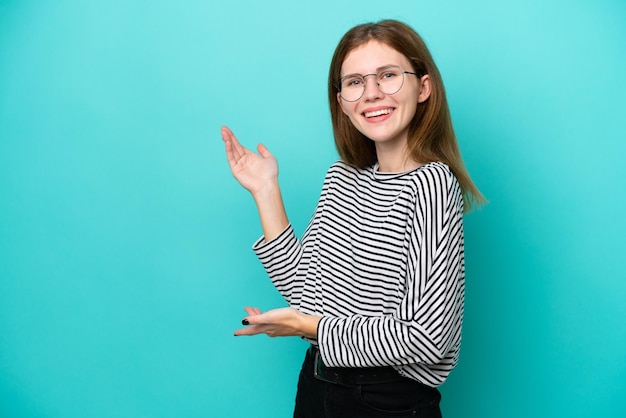 Jonge Engelse vrouw die op blauwe achtergrond wordt geïsoleerd die handen aan de kant uitbreidt om uit te nodigen om te komen