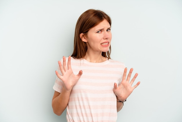 Jonge Engelse vrouw die op blauwe achtergrond wordt geïsoleerd die iemand verwerpt die een gebaar van walging toont.