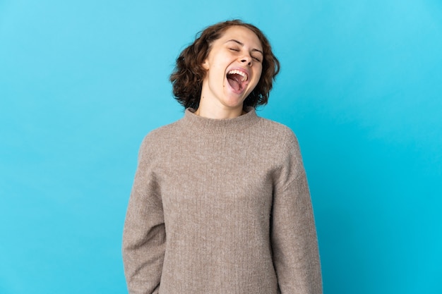 Jonge Engelse vrouw die op blauwe muur het lachen wordt geïsoleerd