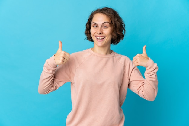 Jonge Engelse vrouw die op blauwe muur wordt geïsoleerd die een duim omhoog gebaar geeft