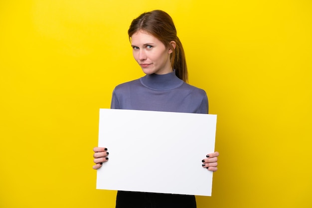 Jonge Engelse vrouw die op gele achtergrond wordt geïsoleerd die een leeg plakkaat houdt